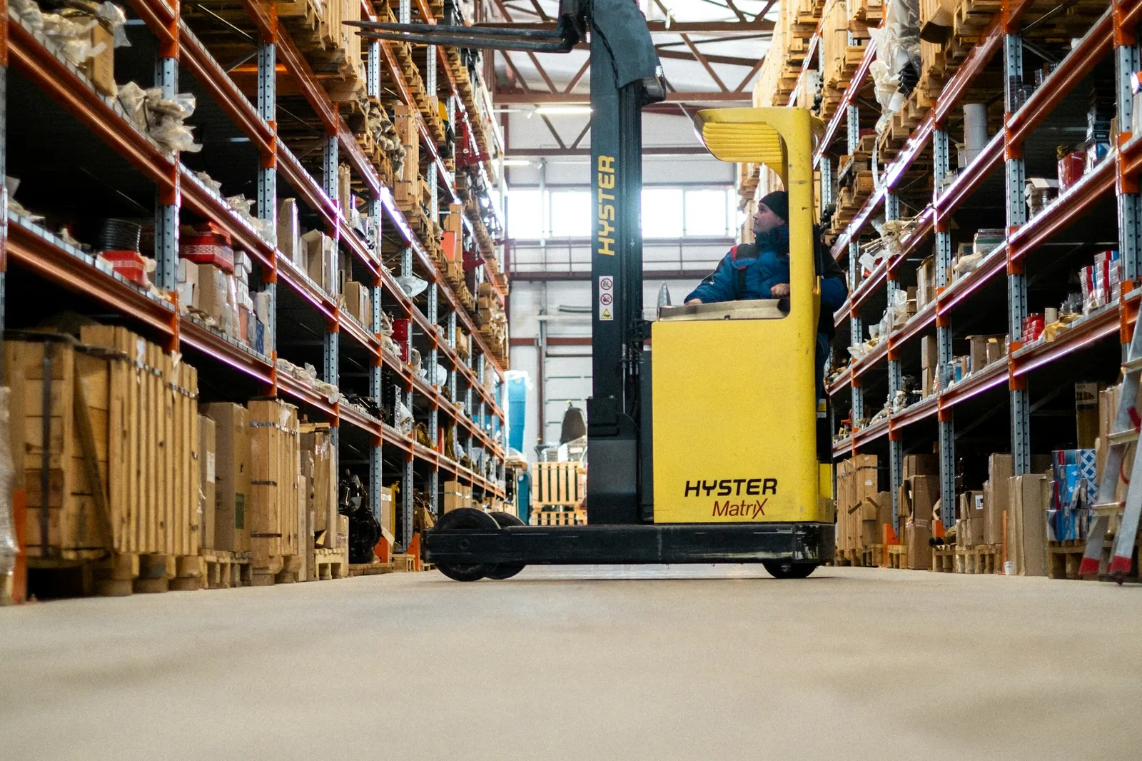 Geniş bir deponun raf koridorunda duran sarı forklift
